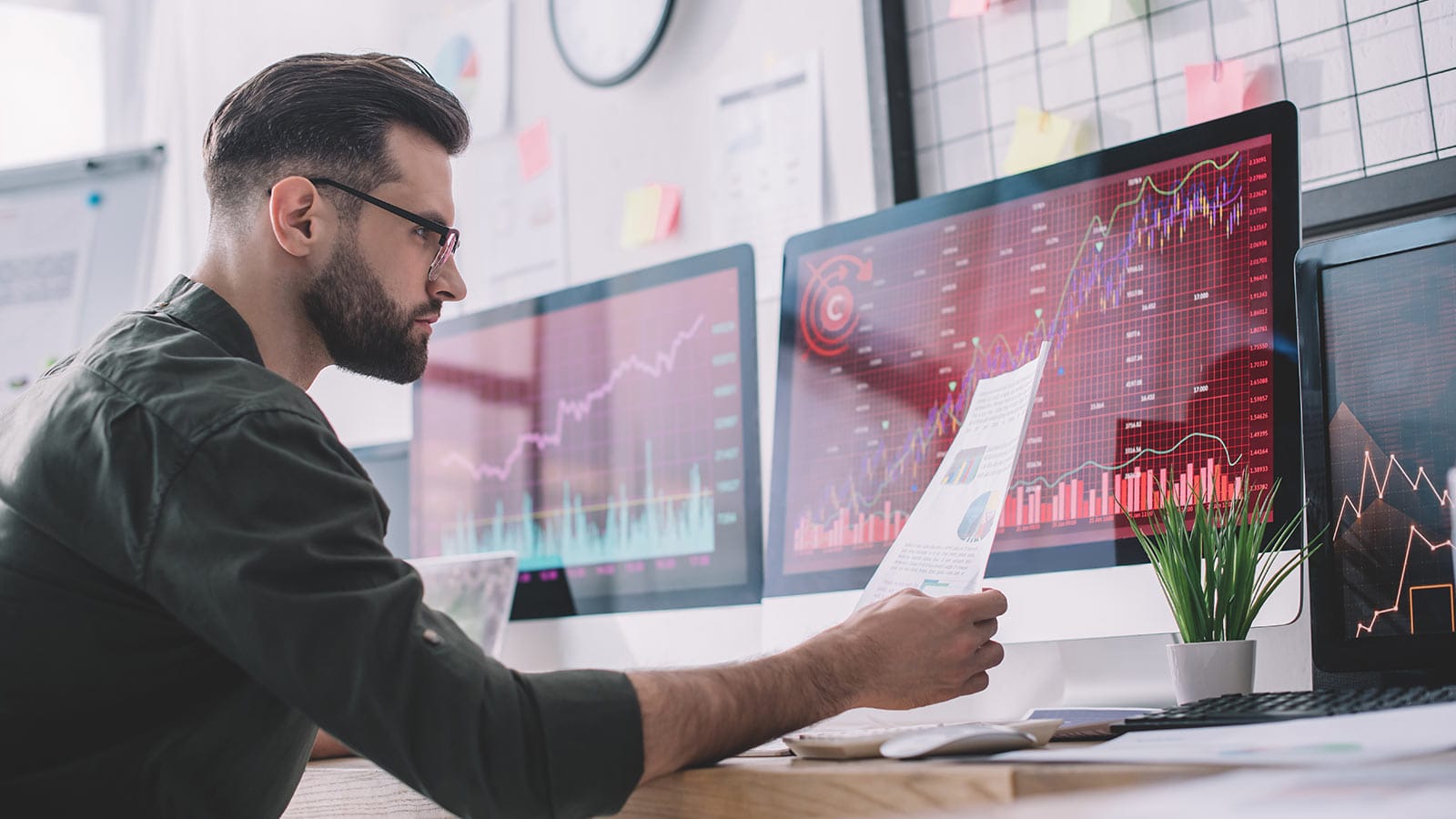 Data analyst που εξετάζει δεδομένα σε οθόνη και χαρτιά
