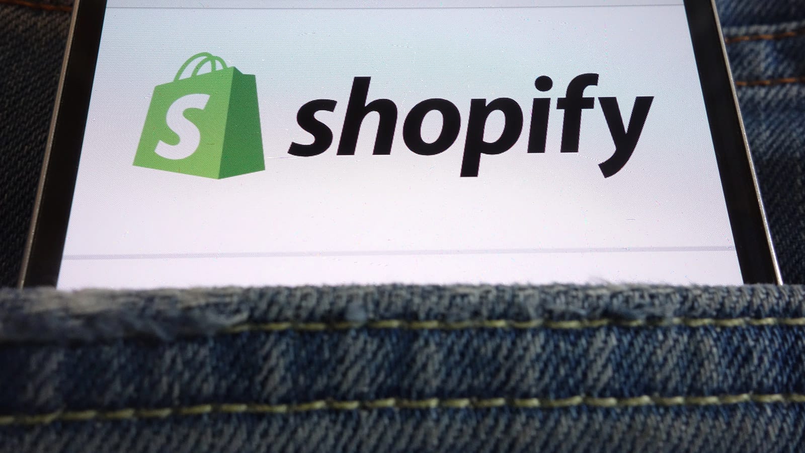 Κινητό σε τσέπη τζιν με το λογότυπο του Shopify