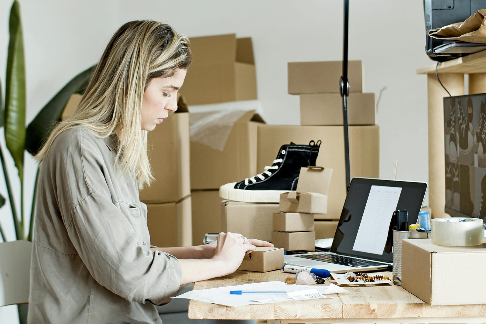 woman in a desk with a pc packing for her online store shoes and boxes