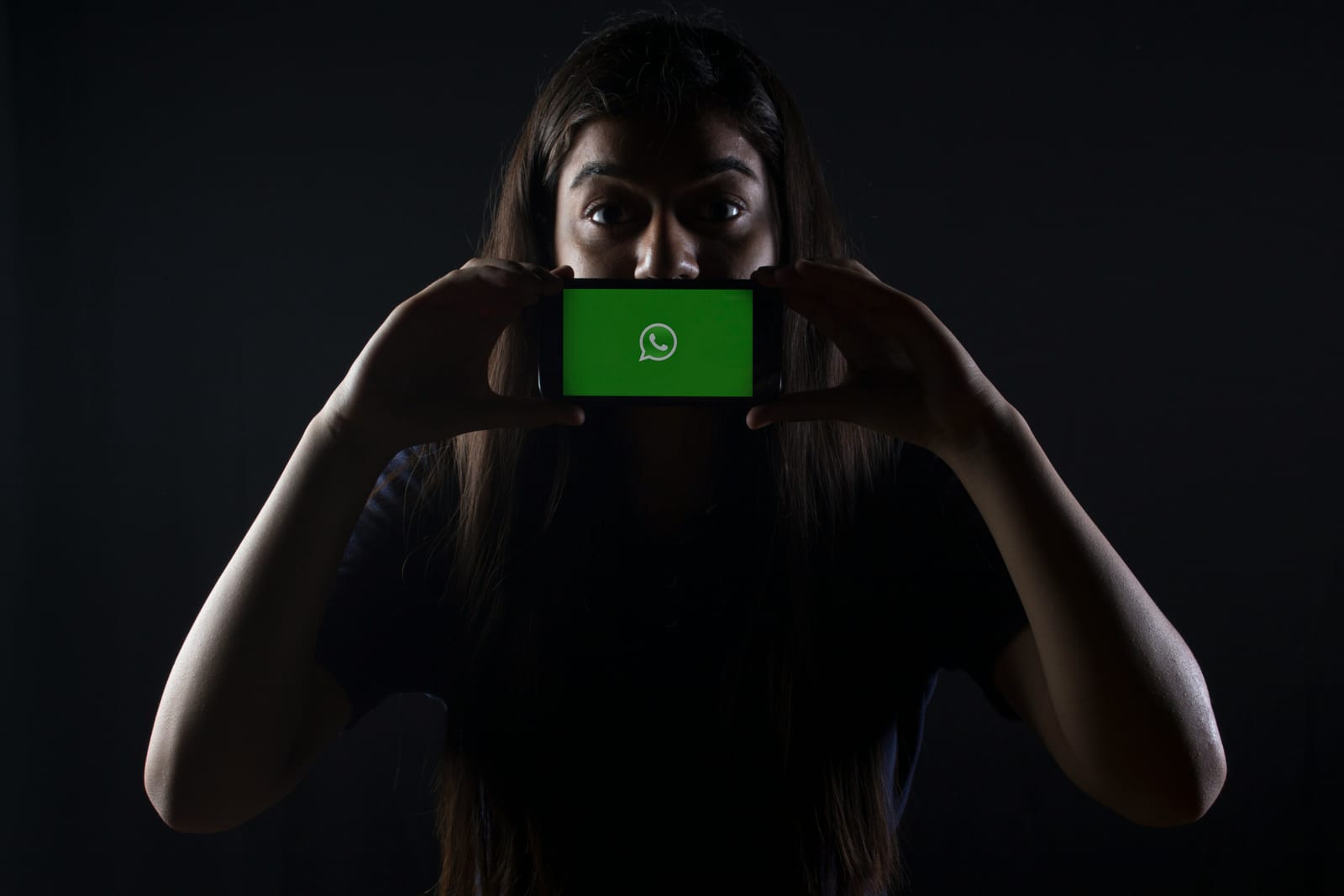girl holding a phone in the dark with WhatsApp in the screen