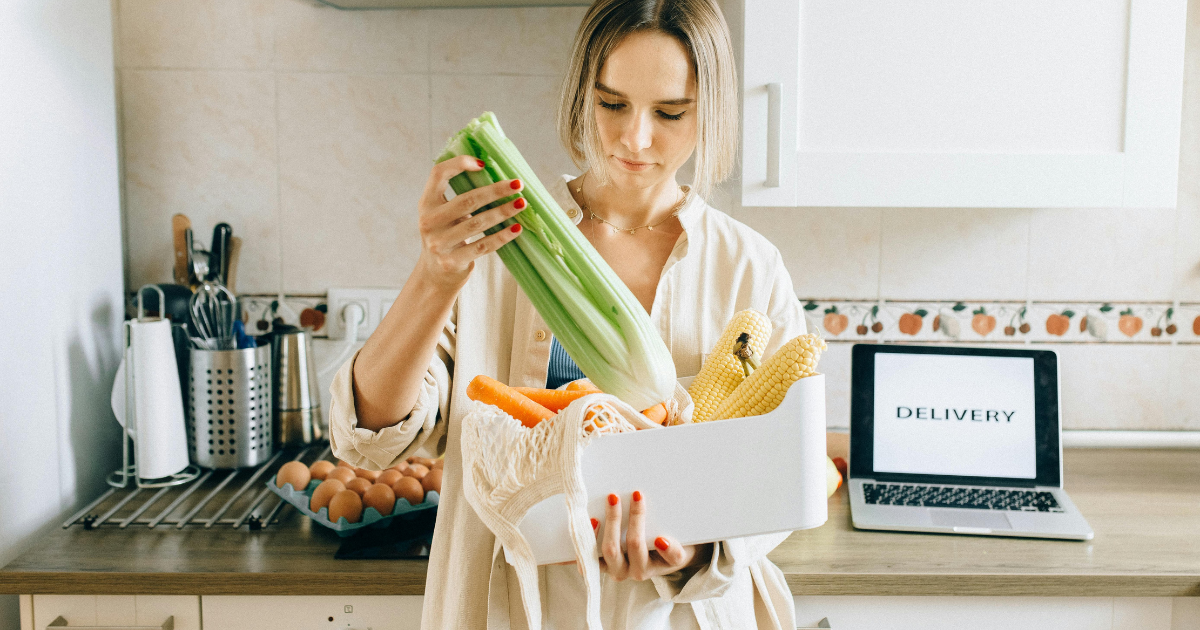 άνθρωπος με eCommerce grocery ψώνια στα χέρια pc στο βάθος κουζίνα
